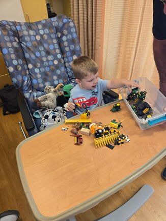 Toddler boy with bandaged fingers plays with toy tractors and farm animals.