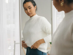 Woman standing in front of mirror wearing casual clothes.