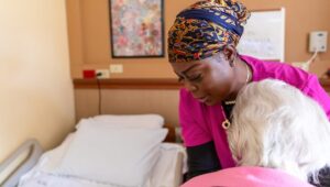 Nursing home nurse helps a senior woman into bed.