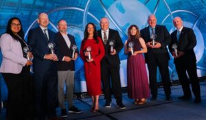 Group of businesspeople holding trophies on stage.