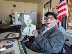 Senior man holds up black-and-white photo of himself as a young soldier.