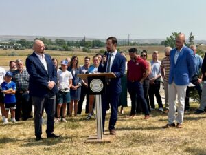 Businessmen make announcement from a podium outside Rapid City, South Dakota, with athletes and other supporters gathered behind them.