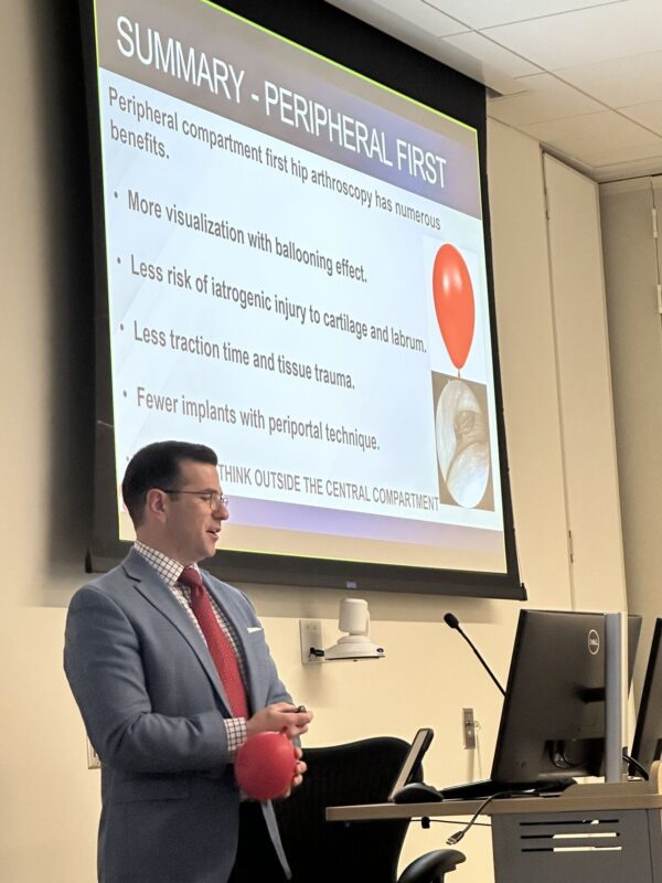 A surgeon gives a slide show while holding a balloon to demonstrate a technique.