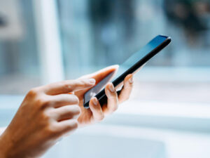 Close up of young woman using a chatbot app on her smartphone at home in sunlight.