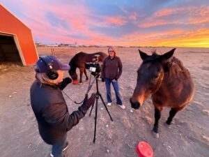 Videographer behind a camera meets with a nurse-rancher and two of her horses at sunrise.
