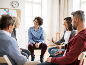 Adults sitting in a circle during group therapy, talking.