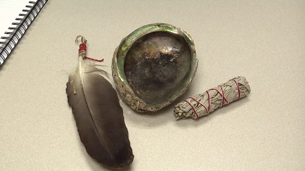 A smudging kit including a feather, shell and sage bundle on a desktop.