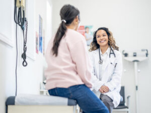A middle aged woman sits up on an exam table as she talks with her doctor about her health concerns.